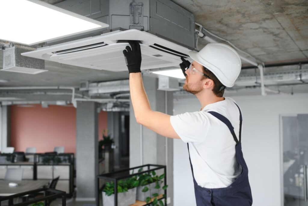 Air conditioning technician inspecting a ceiling-mounted AC unit for maintenance